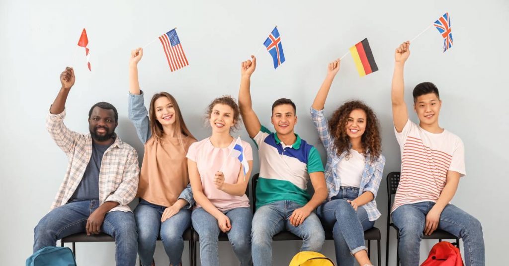 A group of international students sitting in chairs against a wall. Each student holds up a different country's flag.