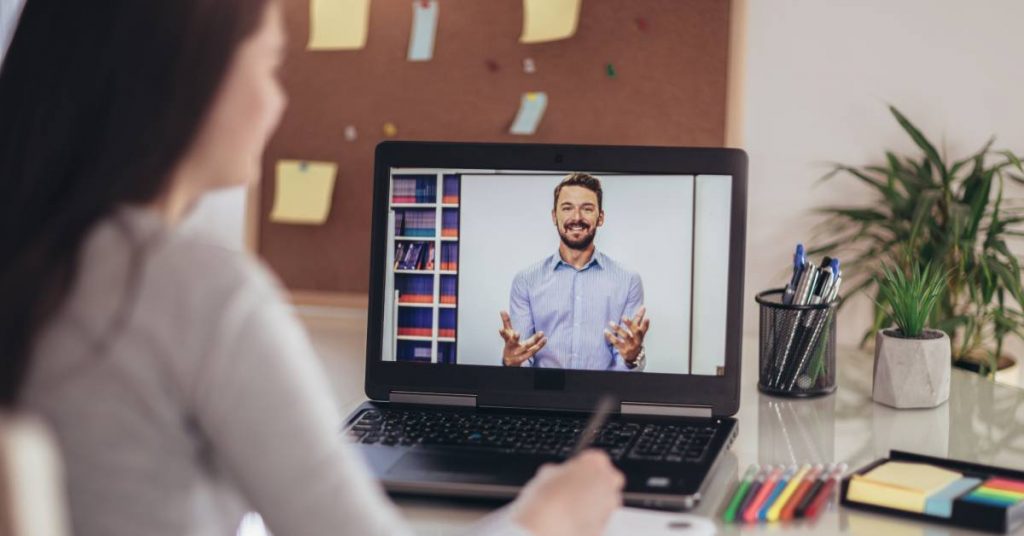 A young student attends an online course. A man on the screen has his hands in front of him, explaining something.