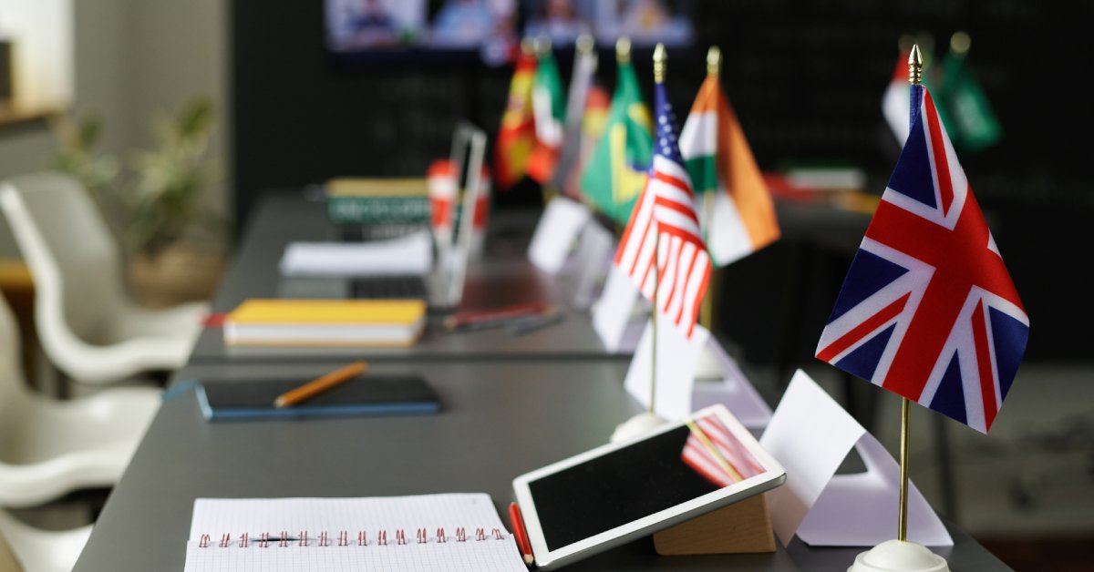 A room with long tables where notebooks, tablets, and flags of different countries sit on the surface.