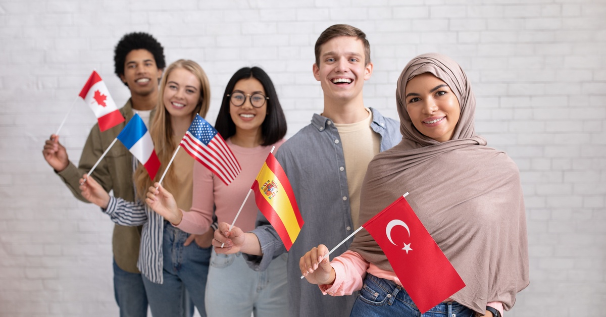 A group of individuals of different ethnicities stand together and smile, as they hold flags of different countries.